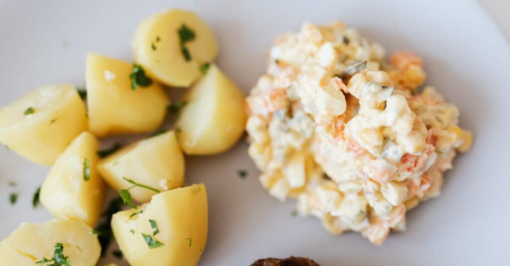 A delectable plate of potato salad with herbs, served alongside boiled potatoes and a meatball, perfect for dinner.